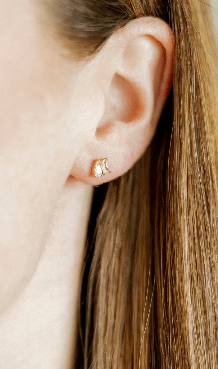 Close-up of an ear wearing a gold earring with a small design.