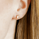 Close-up of an ear wearing a gold earring with a small design.