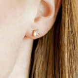 Close-up of an ear wearing a gold earring with a small design.